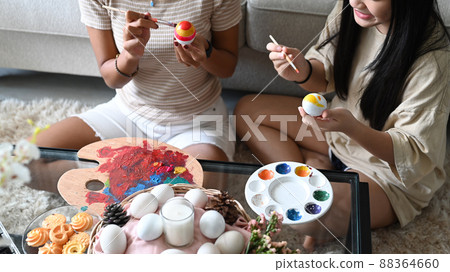 Smiling little girl and mother sitting floor in living room and painting Easter eggs together. Easter, holidays and people concept. 88364660