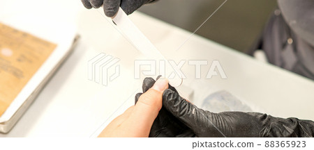 Close up of the caucasian hands of a professional manicurist are filing the nails of a young woman. Young caucasian woman receiving a manicure by a beautician with a nail file in a nail salon Close up of the caucasian hands of a professional manicurist are filing the nails of a young woman. Young caucasian woman receiving a manicure by a beautician with a nail file in a nail salon 88365923