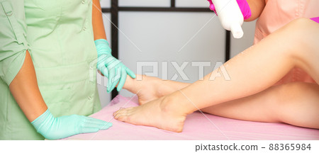 Procedure sugaring. A cosmetologist is sprinkling talcum powder on a young female leg before the depilation procedure Procedure sugaring. A cosmetologist is sprinkling talcum powder on a young female leg before the depilation procedure 88365984
