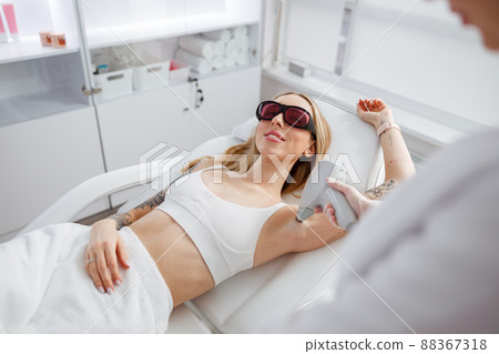 Joyful woman receiving laser epilation treatment in beauty salon 88367318