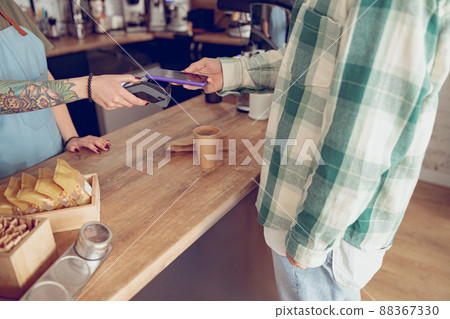 Male customer paying for coffee with smartphone in cafeteria Male customer paying for coffee with smartphone in cafeteria 88367330