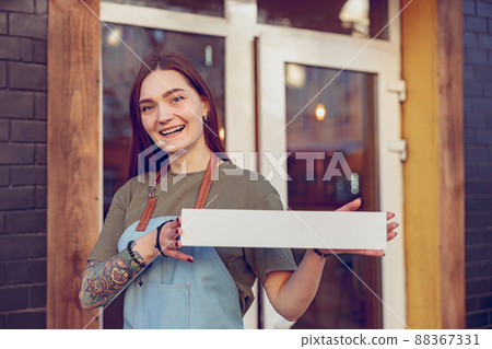 Cheerful female barista with blank signboard standing outdoors Cheerful female barista with blank signboard standing outdoors 88367331
