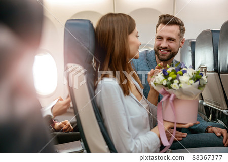 Joyful man and woman with flowers traveling by airplane Joyful man and woman with flowers traveling by airplane 88367377