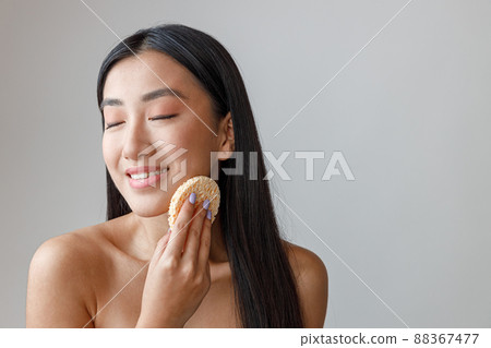 Joyful Asian woman cleaning face with cosmetic sponge Joyful Asian woman cleaning face with cosmetic sponge 88367477