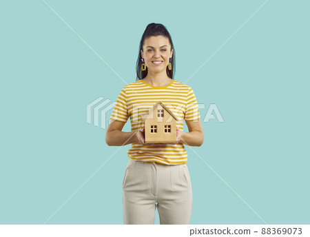 Portrait of pretty smiling woman holding wooden model house standing on blue background. Property investment and house mortgage financial concept. Portrait of pretty smiling woman holding wooden model house standing on blue background. Property investment and house mortgage financial concept. 88369073