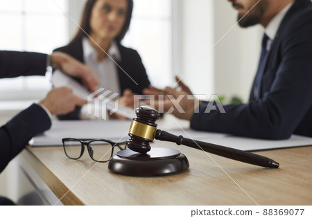 Judge's gavel on table, with lawyer giving legal advice to clients in background Judge's gavel on table, with lawyer giving legal advice to clients in background 88369077
