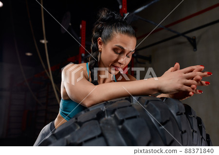 Fit female athlete working out with a huge tire, turning and flipping in the gym. Woman exercising with big tire. 88371840