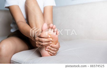 Asian woman sitting on sofa feeling pain in her foot at home 88374525
