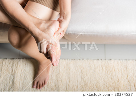 Asian woman sitting on sofa feeling pain in her foot at home 88374527