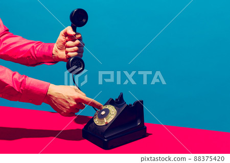 Retro objects, gadgets. Female hand holding handset of vintage phone isolated on blue and pink background. Vintage, retro fashion style. Pop art photography. 88375420