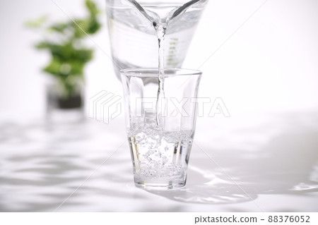 Hands pouring water into a glass of ice 88376052