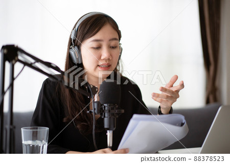 Happy Asian woman setting up a living room in her house for podcast studio, woman arranging a podcast and online radio station at home. Professional young podcaster speaking through a microphone. 88378523
