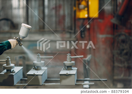 Powder paint coating of metal parts. Worker man in a protective suit sprays powder paint from gun on metal product construction at factory plant. 88379104