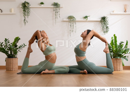 Calm of wellness Couple Asian young woman sit on yoga mat doing breathing exercise yoga  One Legged King Pigeon pose together.Yoga meditation of two healthy female balance body and relax at cozy home 88380101