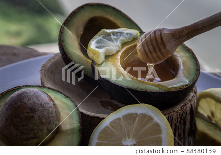 Close-up of Honey dripping from wooden stick dripper into on Fresh organic avocado sliced in half and lemon sliced with honey. 88380139