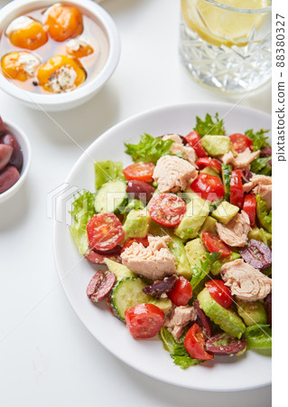 Salad with tuna, lettuce, cucumbers, tomatoes, olives and avocados in white plate on the table 88380327