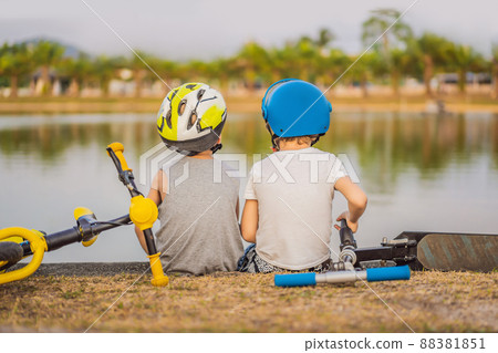 Two boys sit on the shore of the lake after riding a bike and scooter Two boys sit on the shore of the lake after riding a bike and scooter 88381851