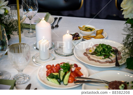 Wedding banquet. The festive table is served with plates with napkins and name cards, glasses and cutlery, and decorated with flower arrangements and candles 88382208
