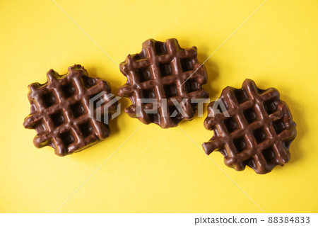 Three chocolate waffles on a yellow background, flat lay, top view. 88384833