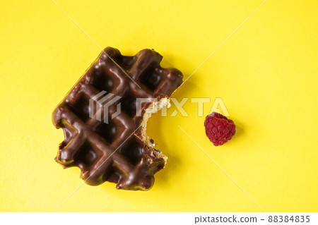 Bitten off chocolate waffle and raspberry, yellow background, top view. 88384835