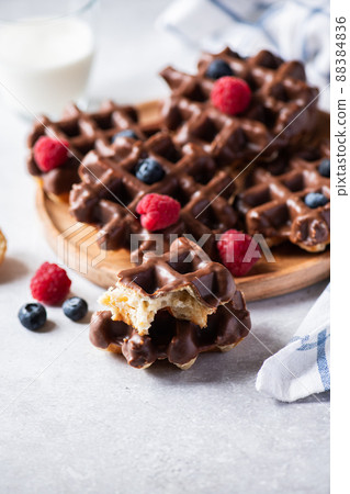 Whole and pieces chocolate waffles, glass of milk on a gray background. Whole and pieces chocolate waffles, glass of milk on a gray background. 88384836