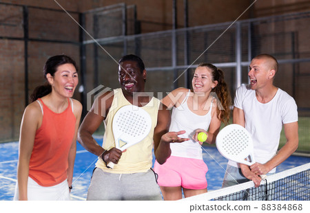 Laughing men and women with rackets and balls talking on indoor padel court 88384868