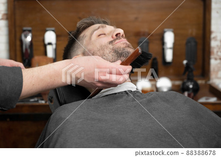 Shot of a barber using a brush on his client's beard Shot of a barber using a brush on his client's beard 88388678
