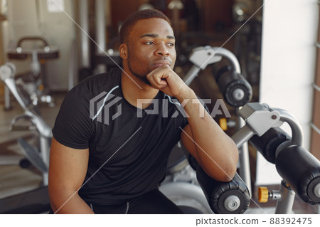 Sports man in the gym. A black man performs exercises. Guy in a black t-shirt Sports man in the gym. A black man performs exercises. Guy in a black t-shirt 88392475