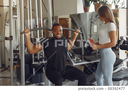 Black man in a gym. Sportspeople in a sportswear. Woman trains black man. 88392477