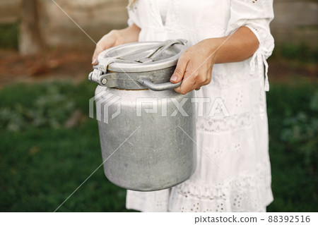 Woman in a summer field. Girl in a white dress. Woman with barrel of milk. 88392516