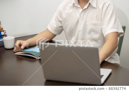 Remote work concept, Male freelancer reading business news on a book and working on laptop at home Remote work concept, Male freelancer reading business news on a book and working on laptop at home 88392774
