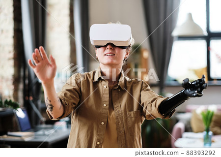 Girl with prosthetic arm gesturing while playing game with VR headset at home Girl with prosthetic arm gesturing while playing game with VR headset at home 88393292