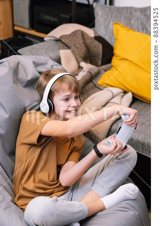 Teen boy actively and recklessly playing video game with joystick sitting on frameless beanbag chair Teen boy actively and recklessly playing video game with joystick sitting on frameless beanbag chair 88394525
