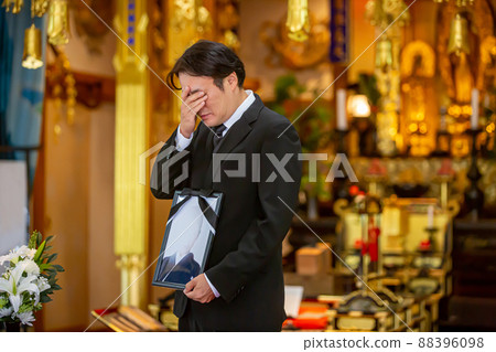 A Japanese male mourner who greets with a portrait of the deceased at a funeral 88396098