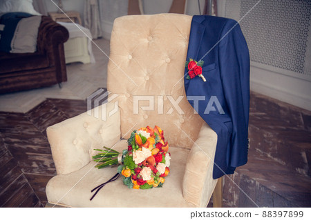 The bride's bouquet and the groom's jacket with a boutonniere on an antique upholstered armchair in the bedroom The bride's bouquet and the groom's jacket with a boutonniere on an antique upholstered armchair in the bedroom 88397899