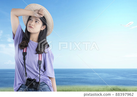 Asian woman with hat and camera standing with unhappy expression Asian woman with hat and camera standing with unhappy expression 88397962