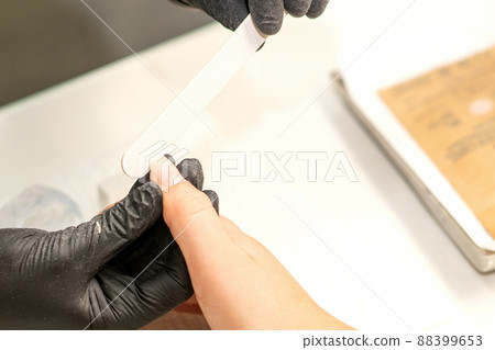 Close up of the caucasian hands of a professional manicurist are filing the nails of a young woman. Young caucasian woman receiving a manicure by a beautician with a nail file in a nail salon Close up of the caucasian hands of a professional manicurist are filing the nails of a young woman. Young caucasian woman receiving a manicure by a beautician with a nail file in a nail salon 88399653
