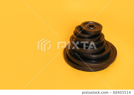 Stack of discs of different weights against yellow background Stack of discs of different weights against yellow background 88403514