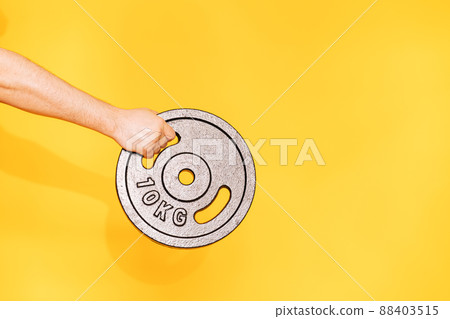 Hand holds ten-kilogram barbell dumbbell against yellow background Hand holds ten-kilogram barbell dumbbell against yellow background 88403515