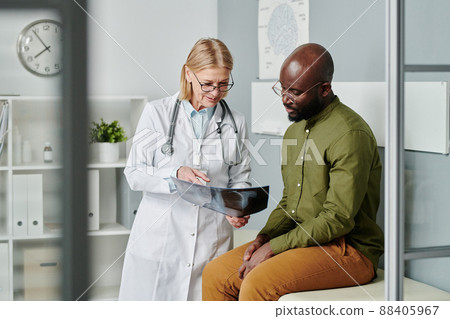 Confident mature doctor in whitecoat showing young black man x-ray image 88405967