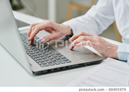 Hands of mature female clinician pressing buttons of laptop keyboard by desk Hands of mature female clinician pressing buttons of laptop keyboard by desk 88405979