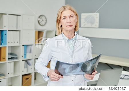 Mature blond female radiologist in whitecoat holding x-ray image of lungs 88405987