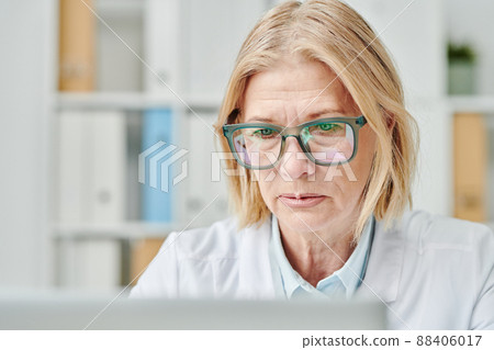 Contemporary mature online doctor looking at computer screen in office 88406017