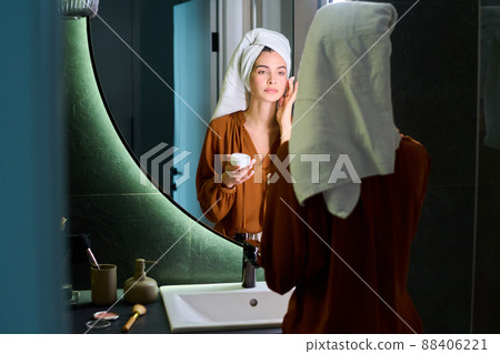 Young beautiful woman applying moisturizing cream on her face after bath Young beautiful woman applying moisturizing cream on her face after bath 88406221