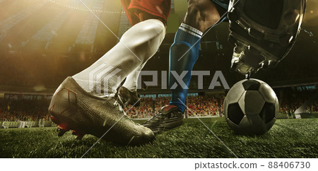 Close-up legs of soccer, football players in action, motion at the stadium with flashlights and crowded stands. Concept of sport, competition, movement, overcoming. Close-up legs of soccer, football players in action, motion at the stadium with flashlights and crowded stands. Concept of sport, competition, movement, overcoming. 88406730