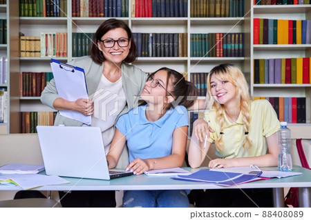 Girls teenage students studying in library with teacher mentor Girls teenage students studying in library with teacher mentor 88408089