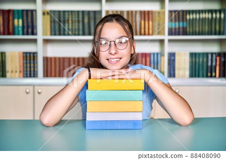 Smiling schoolgirl looking at the camera, with stack of books 88408090