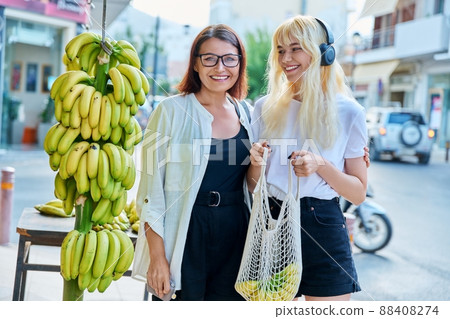 Mother and teenage daughter buying bananas at a street retail market 88408274