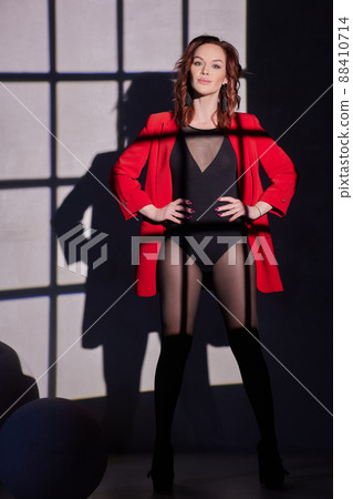 Fashion photo of a beautiful elegant young asian woman in a pretty red oversized suit, jacket, pants posing over white, soft gray background. Fashion photo of a beautiful elegant young asian woman in a pretty red oversized suit, jacket, pants posing over white, soft gray background. 88410714