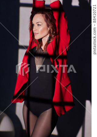 Fashion photo of a beautiful elegant young asian woman in a pretty red oversized suit, jacket, pants posing over white, soft gray background. 88410721